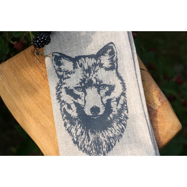 Frohstoff Nahaufnahme der Serviette aus Leinen mit Fuchs Motiv auf einem Hocke aus Holz neben einem Beerenbusch zusammengelegt