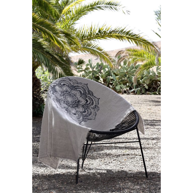 Frohstoff Plaid aus Leinen mit Ornament Motiv in Pastellanthrazit über einen Stuhl gelegt, der sich vor einer Palme befindet