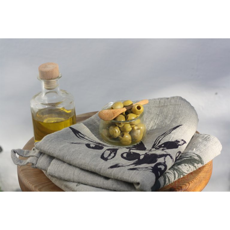 Frohstoff Geschirrtuch aus Leinen Natur mit Oliven und Chili Motiv zusammengelegt und dekoriert mit einer Schale gefüllt mit Oliven und einer Flasche Olivenöl auf einem hölzernen Hocker