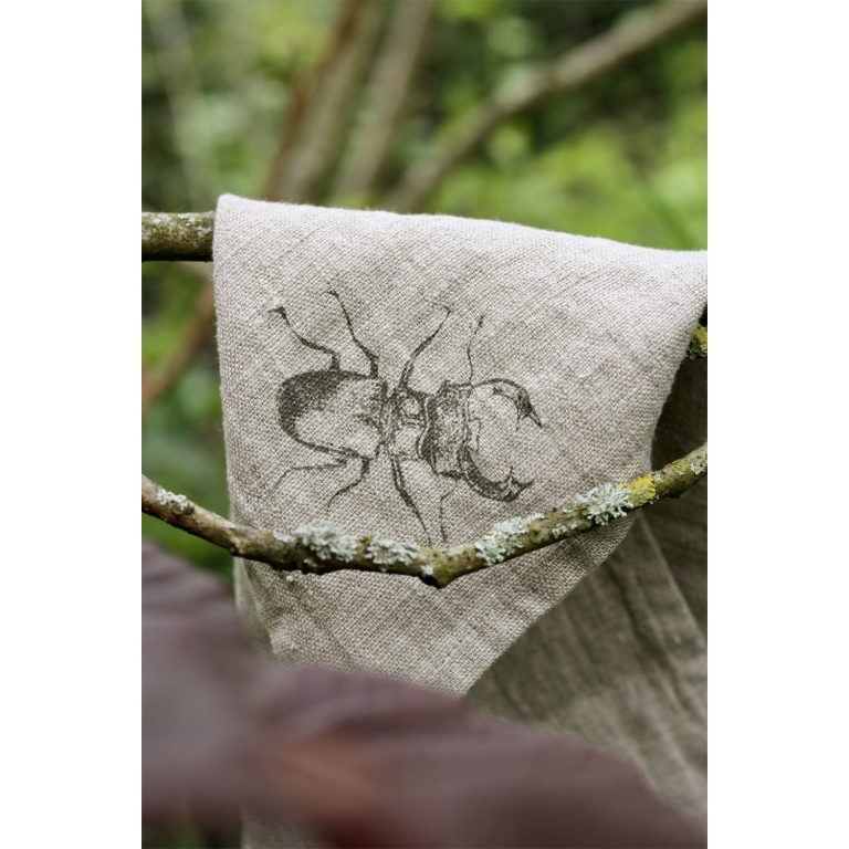 Frohstoff Serviette aus Leinen mit Käfer Motiv auf einen Ast eines Baumes gehängt