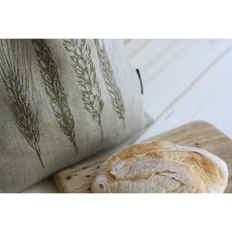 Frohstoff Brotbeutel aus Leinen mit Ähren Motiv in Olivgold neben einen Holzbrett mit einem Brot angerichtet