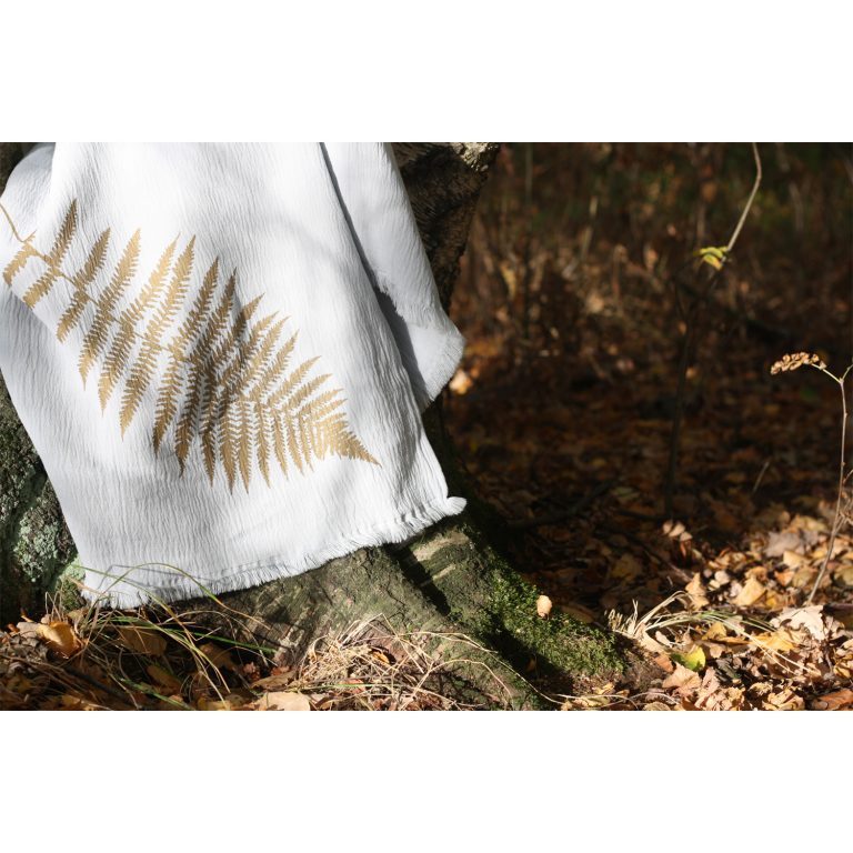 Frohstoff graue Decke mit Farn Motiv als nahaufnahme des Motiv über den Stamm eines Baumes gelegt mit Herbstlaub am Boden