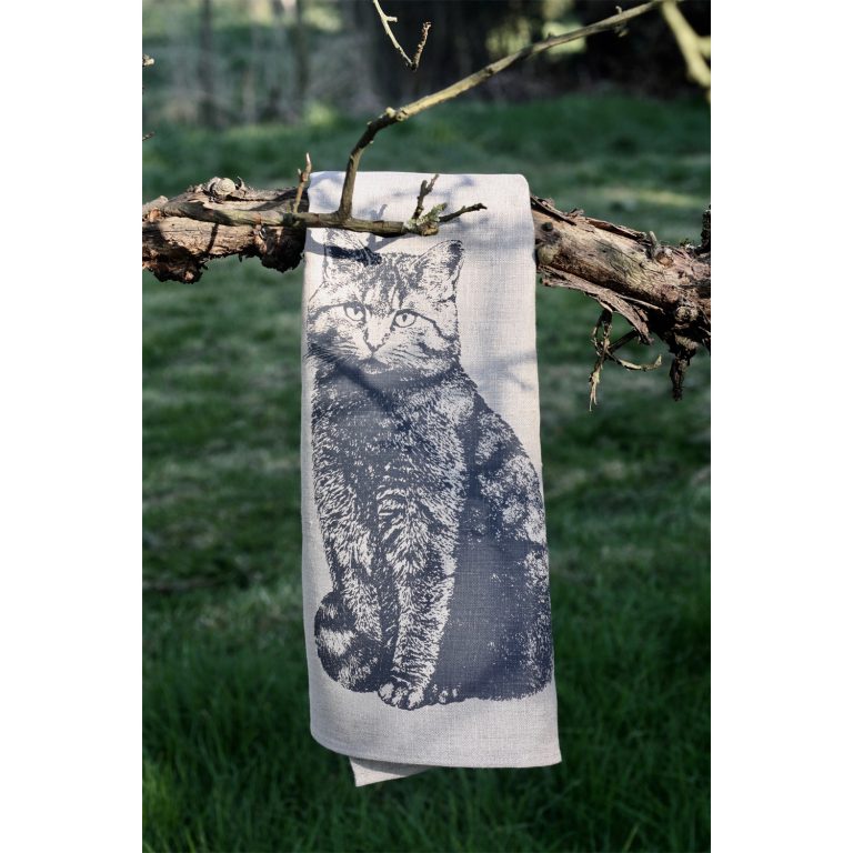 Frohstoff Geschirrtuch aus Leinen mit dem Wildkatzen Motiv über einen Ast gelegt. Im Hintergrund ist eine Rasenfläche
