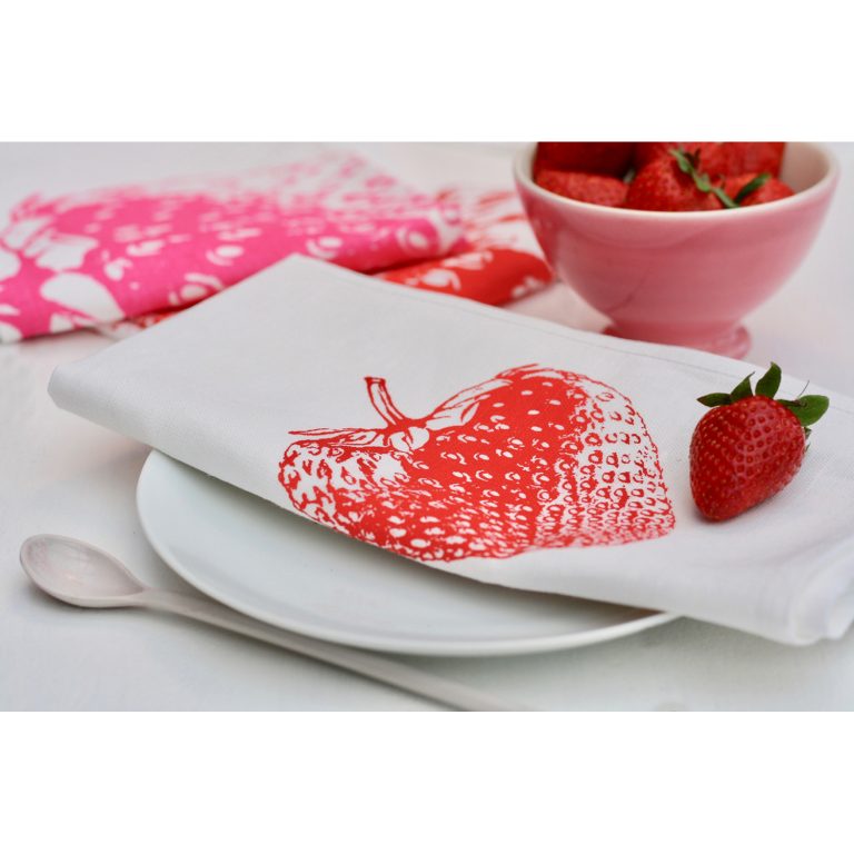 Frohstoff Serviette mit Erdbeeren Motiv in Rot auf einem Teller zusammengelegt mit einer Erdbeere darauf mit einer rosanen Schale mit Erdbeeren gefüllt