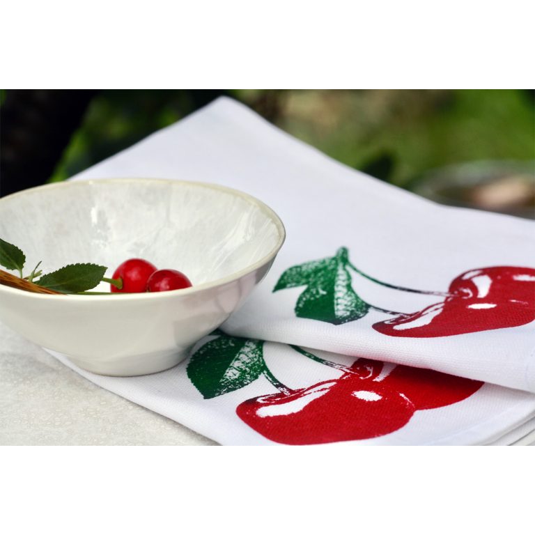 Frohstoff Servietten mit Kirsch Motiv in rot-grün auf einen Teller zusammengelegt mit einer grauen Schale gefüllt mit 2 Kirschen