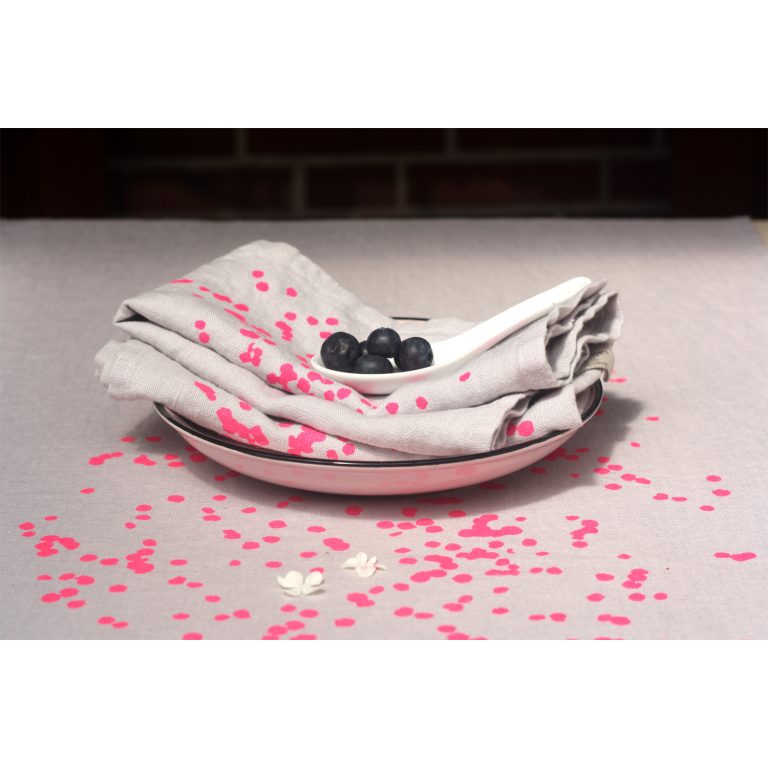 Frohstoff Tischläufer aus Leinen Grau mit Blütenblätter Motiv in neonpink mit den dazu passenden Servietten in einem Teller zusammengelegt mit einem weißen Porzellan Löffeln mit Beeren angerichtet