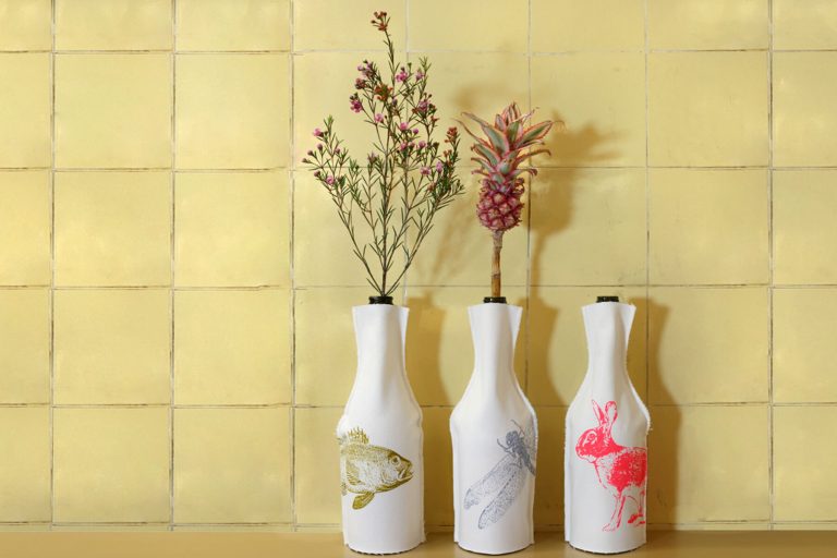 Frohstoff Flaschenhusse mit Barsch Libellen und Hasen Motiv dekoriert mit Pflanzen vor einer gelb gefliesten Wand