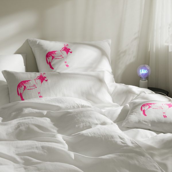 Frohstoff verschiedene Kissen mit Esel-Motiv in Neon-pink dekoriert auf einem Bett un einer Lampe