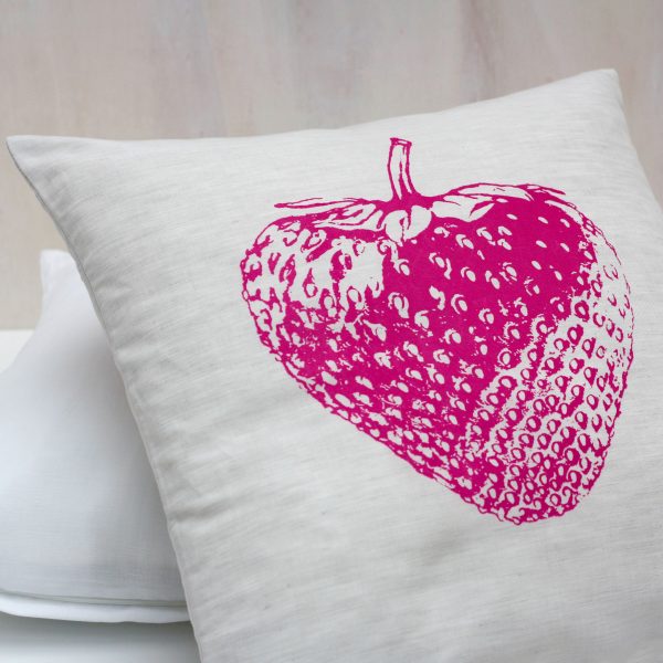 Frohstoff Kissen mit pinken Erdbeeren-Motiv auf einem weiteren Kissen, dahinter eine helle Holzwand