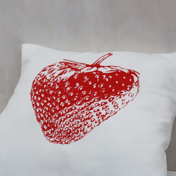 Frohstoff Kissen mit roten Erdbeeren-Motiv an eine Holzwand gelehnt