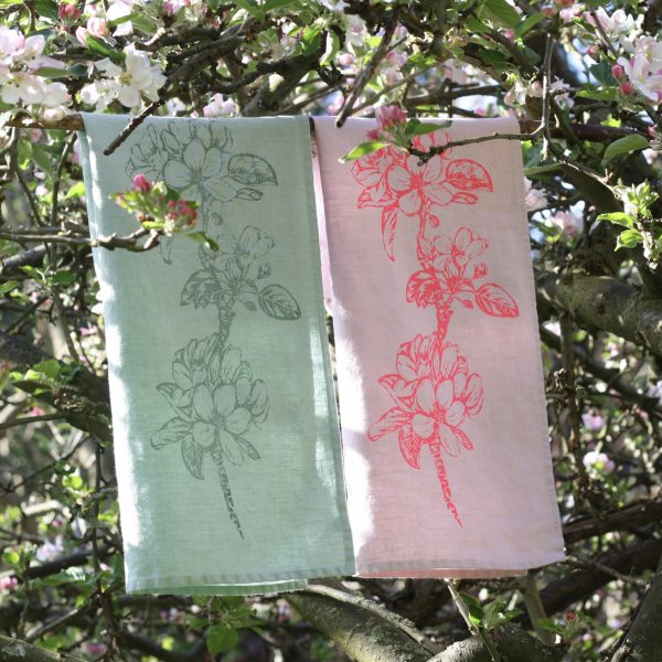 Frohstoff Geschirrtuch mit Apfelblütenzweig-Motiv in Minze und Rosa in einem blühenden Apfelbaum aufgehangen